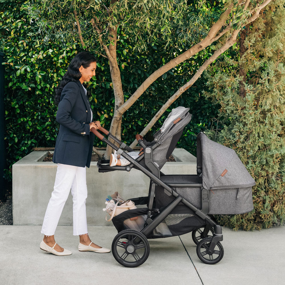 Woman pushes baby in UPPAbaby Bassinet V3 - GREYSON (Charcoal Melange) and toddler in toddler seat on UPPAbaby VISTA V3 Stroller - GREYSON (Charcoal Melange)