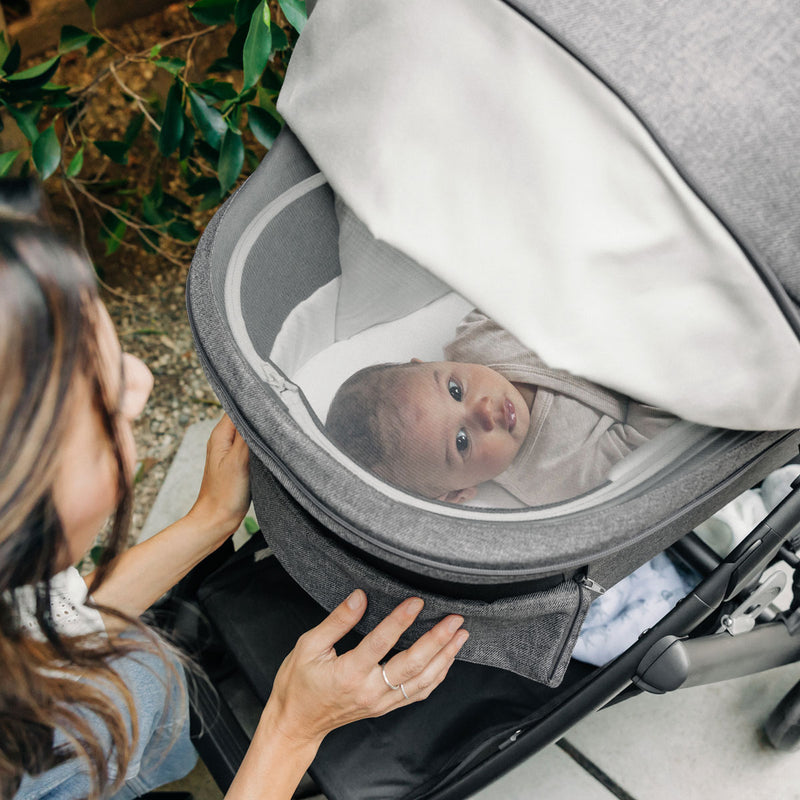 Mom checks on baby lying in UPPAbaby Bassinet V3 - GREYSON (Charcoal Melange)