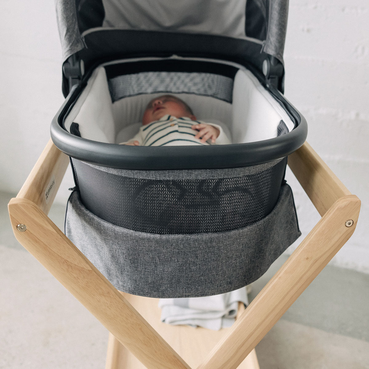 Baby lies in bassinet attached to UPPAbaby New Bassinet Stand - Natural