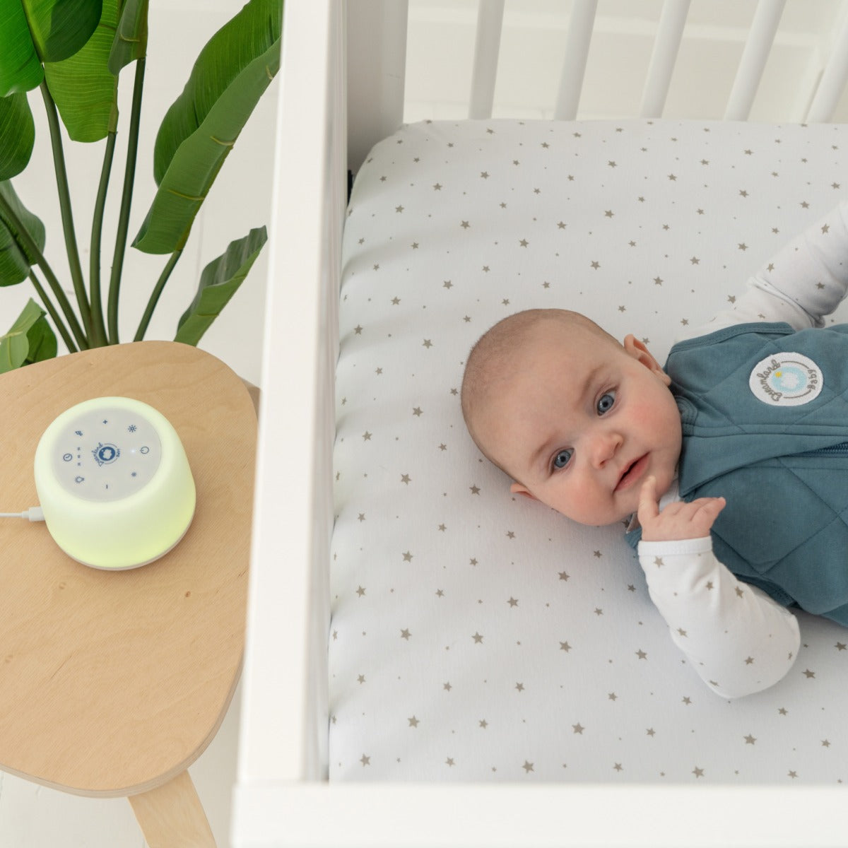 Dreamland Baby Dream Sound Machine - White next to baby in crib