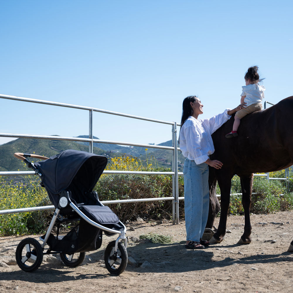 Mom holds baby on horse while standing next to Bumbleride 2024 Indie All Terrain Stroller - Dusk