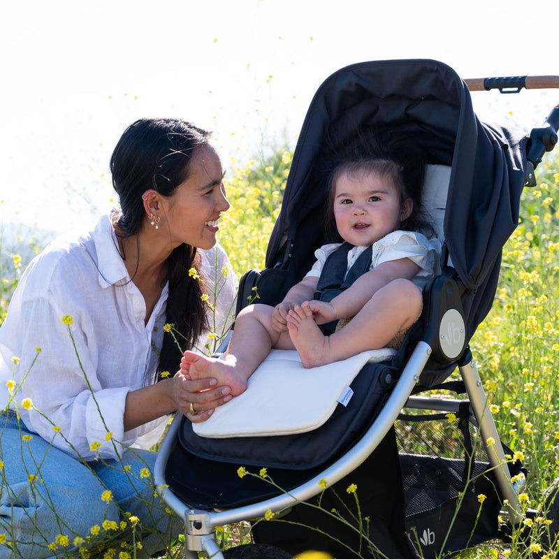 Mom holding flowers smiles at baby sitting in Bumbleride 2024 Indie All Terrain Stroller - Dusk