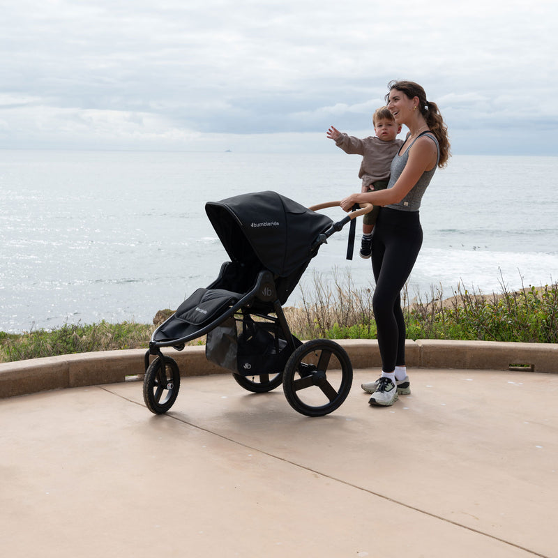 Mom holds toddler while holding handlebar of Bumbleride 2024 Speed Jogging Stroller - Black