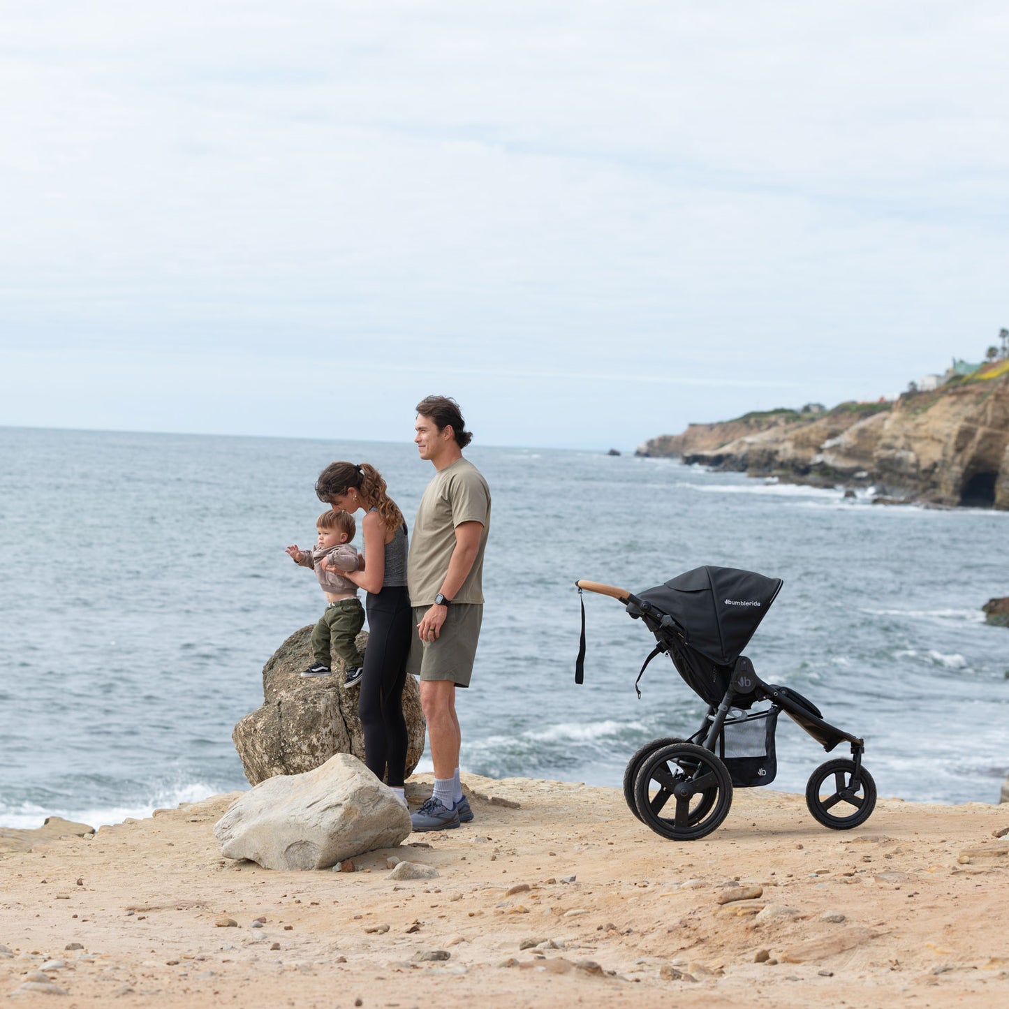 Family stand on beach looking at ocean with Bumbleride 2024 Speed Jogging Stroller - Black nearby