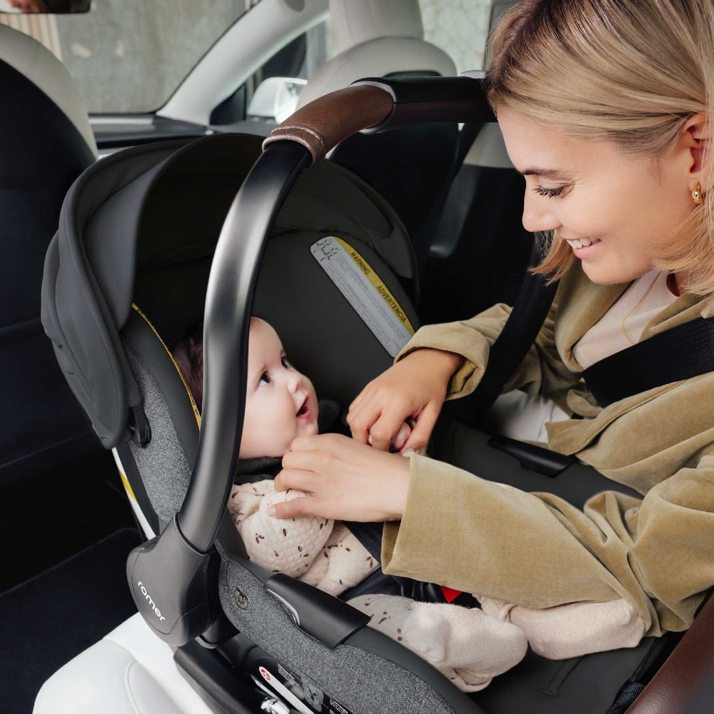 Woman sits in backseat next to baby in Romer Juni Infant Car Seat - Peppercorn