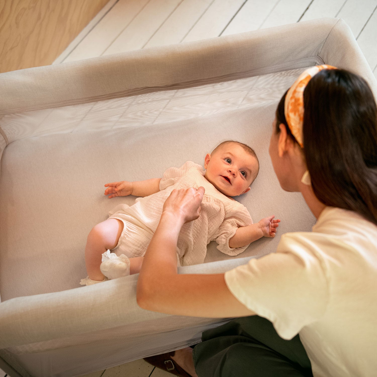 Mom looks at baby in bassinet attachment of Nuna PAAL Play Yard - Biscotti