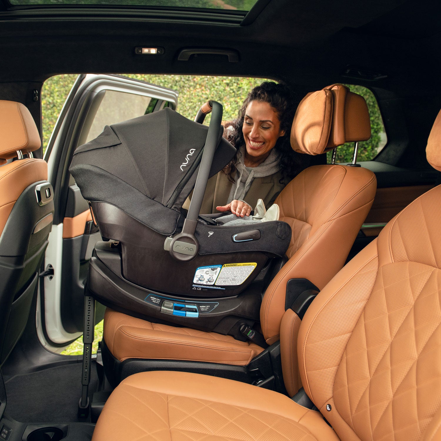 Mom placing baby into vehicle inside infant car seat of Nuna DEMI Next Stroller and PIPA Aire RX Car Seat Travel System - Caviar