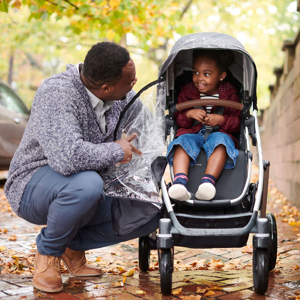 Dad checks on child sitting in VISTA V2 stroller with UPPAbaby VISTA / VISTA V2 / CRUZ / CRUZ V2 Performance Rain Shield attached