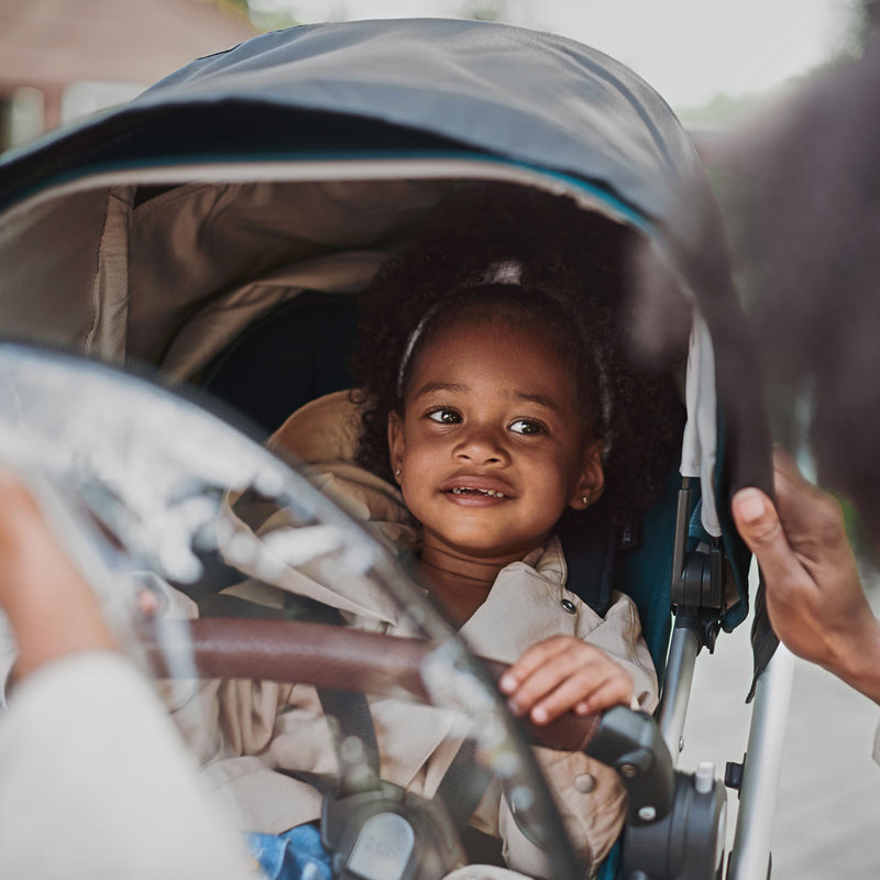 Child sitting in CRUZ stroller with attached UPPAbaby VISTA / VISTA V2 / CRUZ / CRUZ V2 Performance Rain Shield