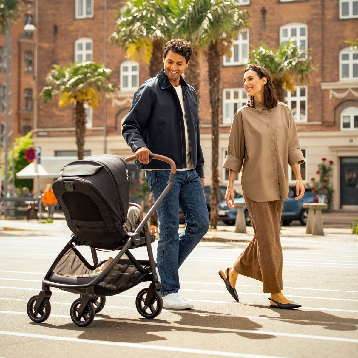 Man walks next to woman while pulling Nuna SWIV Stroller - Caviar