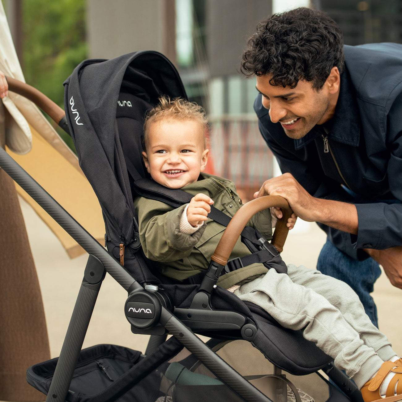 Man smiles at toddler boy sitting in Nuna SWIV Stroller - Caviar