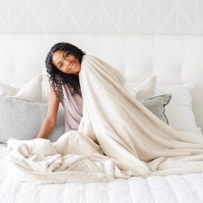 Woman sits on bed while using Saranoni Lush XL Blanket - Buttermilk