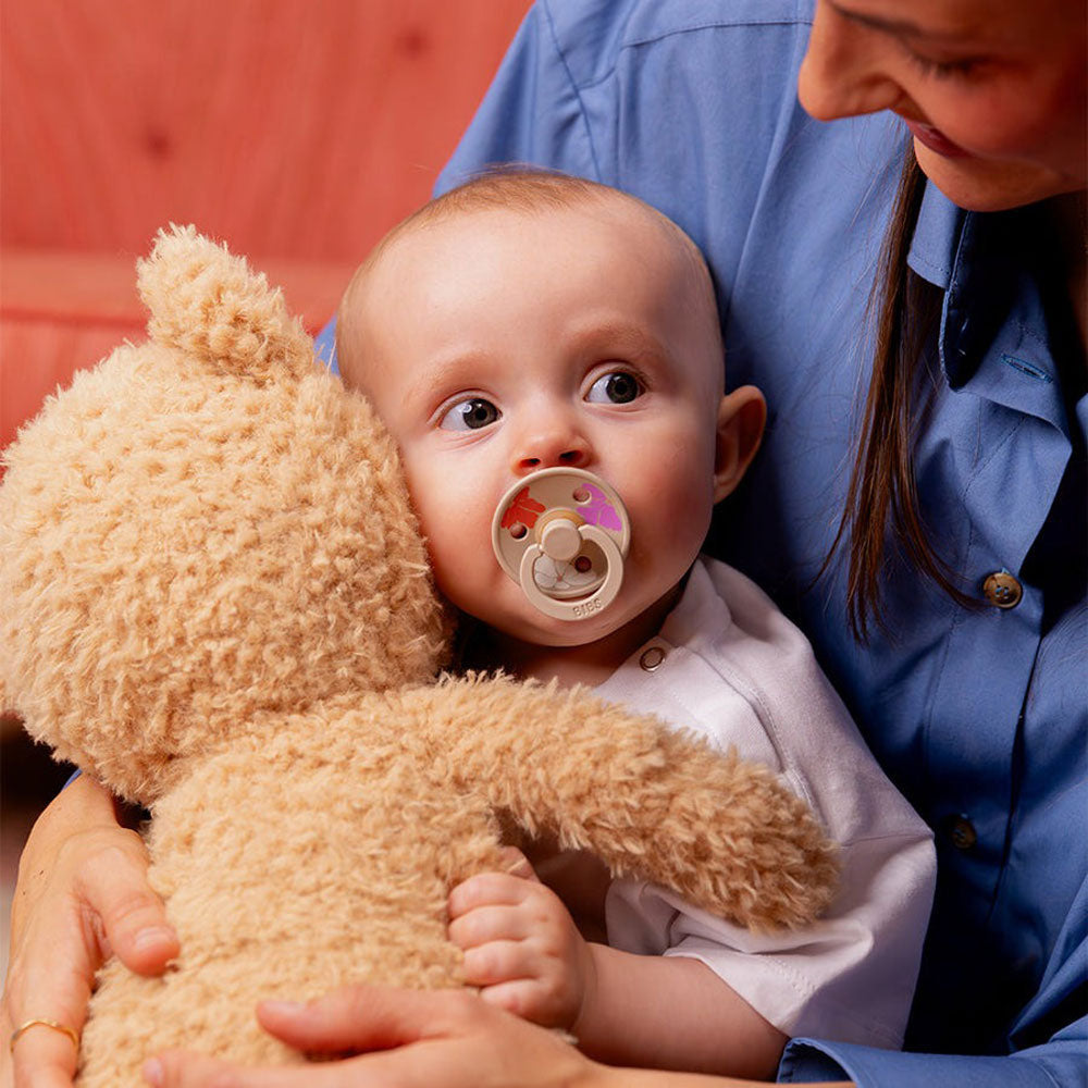 Baby holds teddy bear while sucking on BIBS Studio Colour 2-Pack Pacifier Set - Morning Bloom - Ivory Mix