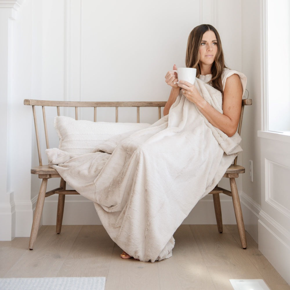 Woman holds a mug while sitting on a bench using Saranoni Lush XL Blanket - Buttermilk