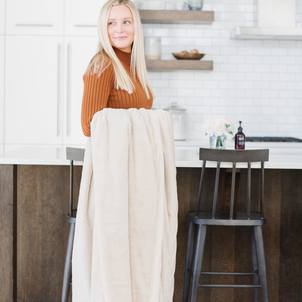 Woman stands in kitchen while holding Saranoni Lush XL Blanket - Buttermilk